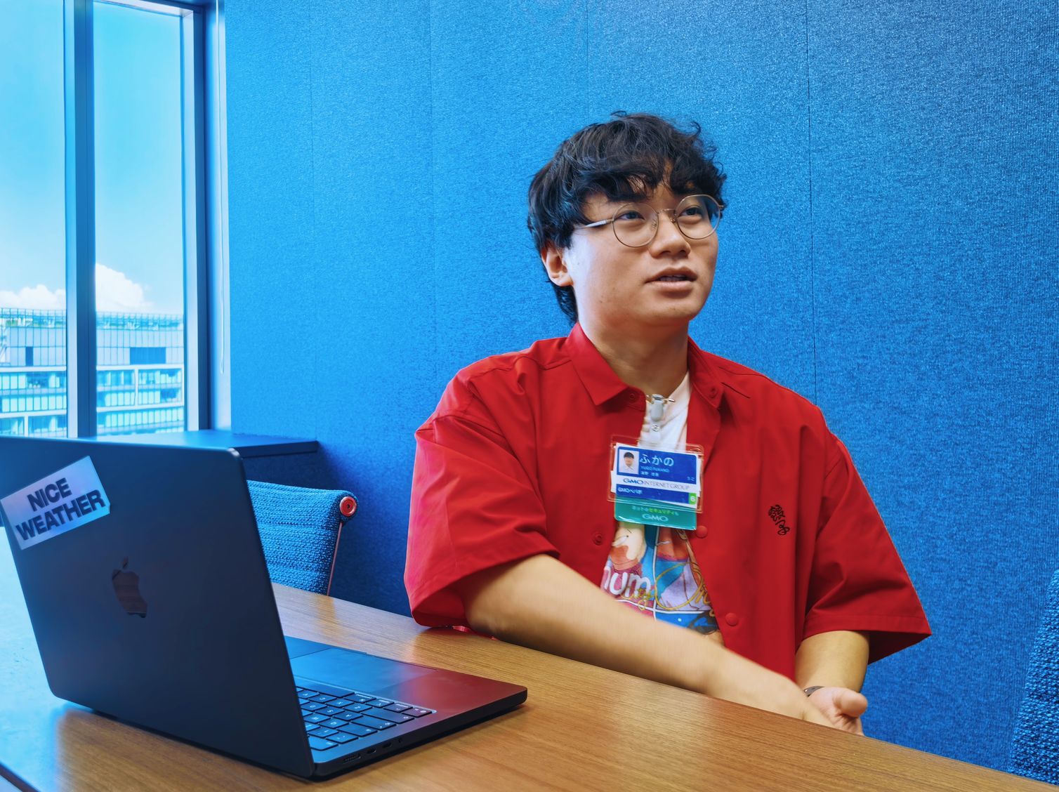インタビュー中の深野悠吾さん。青い壁の会議室でノートPCの前に座り、やや上を見ながら開発体制やCLI提供の経緯について語っている